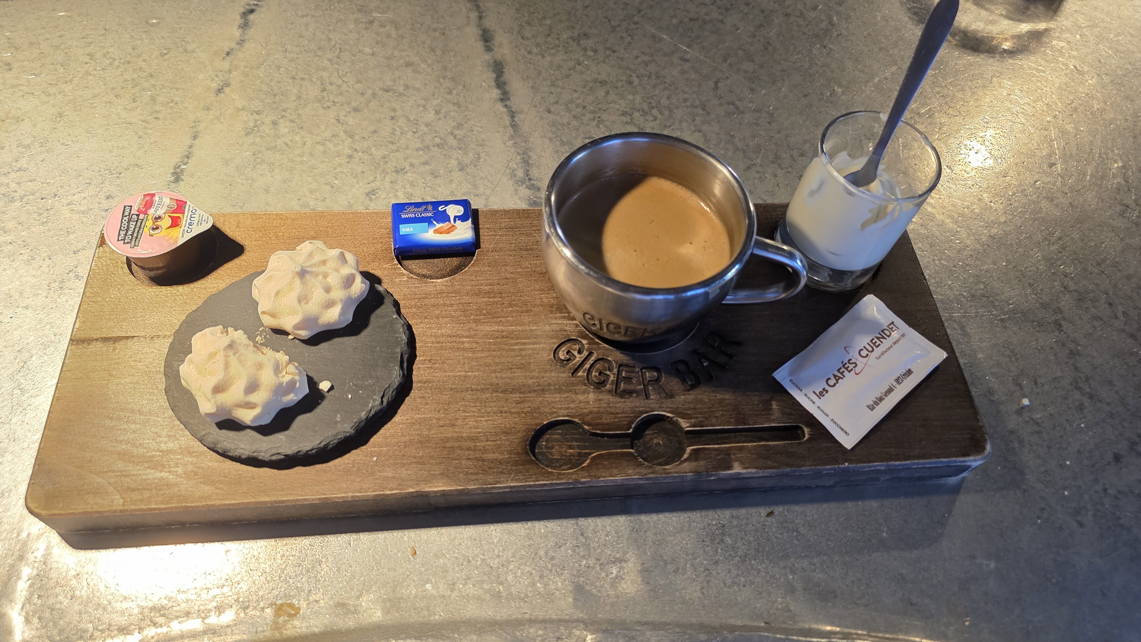 Coffee served on a branded Giger Bar wooden tray with mini meringues at the HR Giger Museum bar in Gruyères