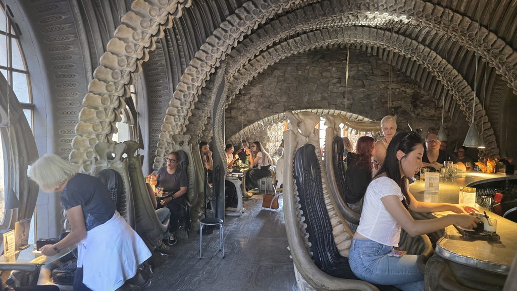 Guests seated in bone-shaped chairs under the vertebrae arch ceiling inside the HR Giger Bar in Gruyères