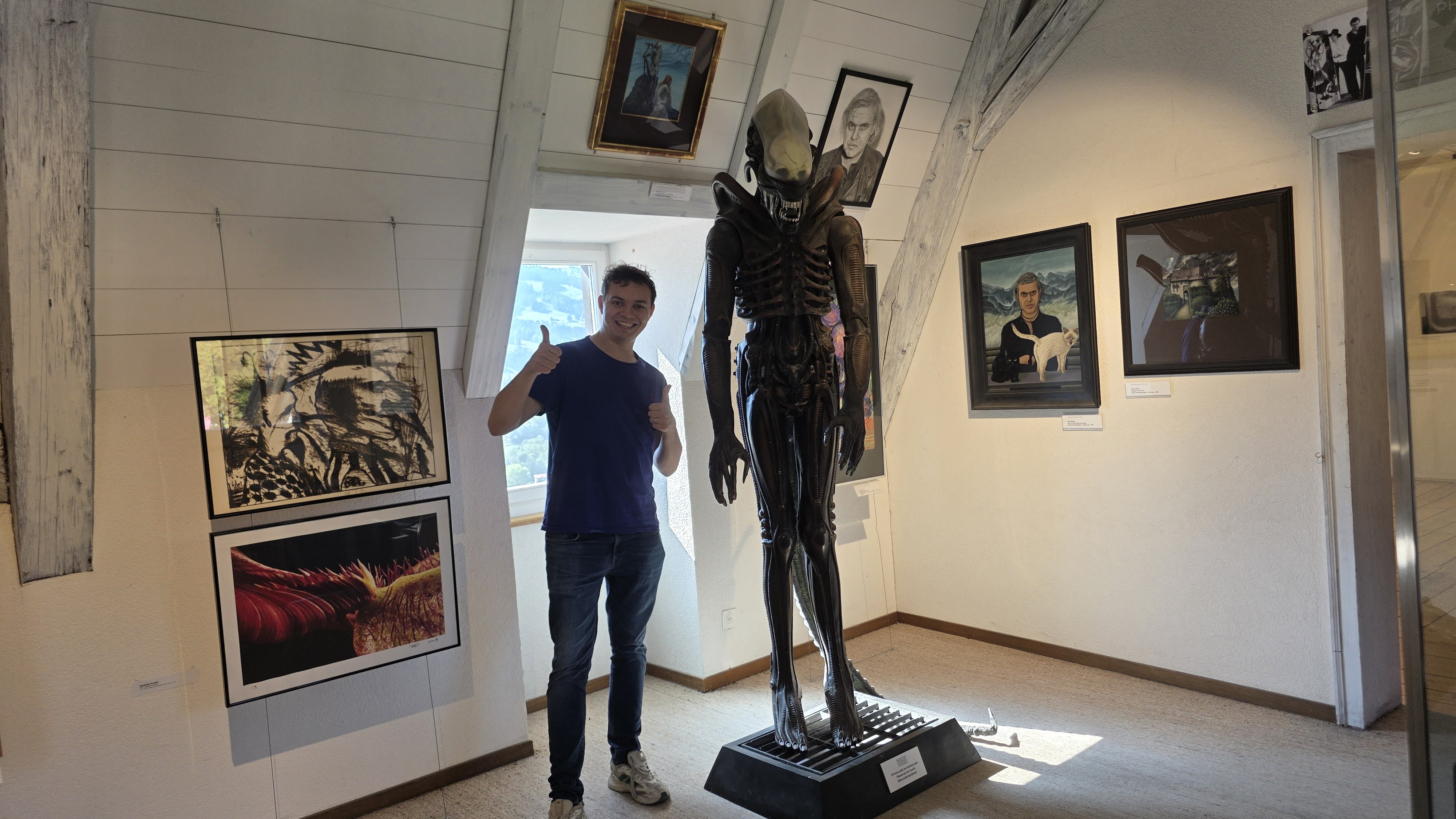 Visitor giving thumbs up next to a life-size Alien creature sculpture at the HR Giger Museum in Gruyères